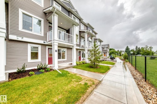 Modern townhouse exterior featuring horizontal siding, white trim, red entry doors, and individual balconies - 17 4137 76 Street, Edmonton, AB 