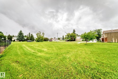 Expansive green space featuring a grass field, mature trees, and a black chain-link fence - 17 4137 76 Street, Edmonton, AB 