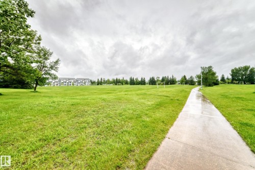 Expansive green space featuring a concrete pathway, mature trees, distant multi-story residential buildings, and athletic field goalposts - 17 4137 76 Street, Edmonton, AB 