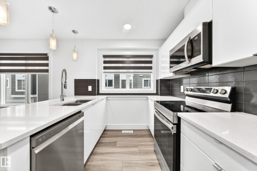 Contemporary kitchen featuring white flat-panel cabinetry, light-toned countertops, stainless steel appliances, and a dark subway tile backsplash - 17 4137 76 Street, Edmonton, AB 