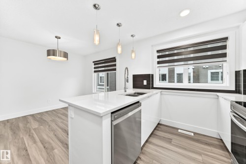 Modern kitchen featuring an island with a stainless steel dishwasher, white countertops, coordinating white cabinetry, and wood-finish flooring - 17 4137 76 Street, Edmonton, AB 