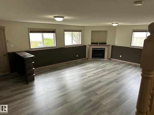 Spacious room featuring wood-finish flooring, multiple windows, and a corner-set fireplace with a mantle - 1978 Tomlinson Green Green, Edmonton, AB 