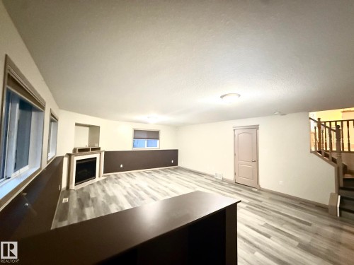 Spacious room featuring wood-finish flooring, a built-in fireplace with a mantel, and multiple windows - 1978 Tomlinson Green Green, Edmonton, AB 