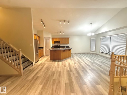 Open-concept living area featuring wood-finish flooring, a kitchen island with seating, stainless steel appliances, and vaulted ceilings - 1978 Tomlinson Green Green, Edmonton, AB 