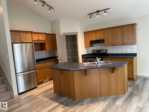 Kitchen featuring wood-finish cabinetry, stainless steel appliances, central island with double basin sink, track lighting, and wood-finish flooring - 1978 Tomlinson Green Green, Edmonton, AB 