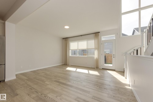 Spacious interior featuring light wood-finish flooring, a large window with roller shades, and a glass-paneled exterior door - 3249 Dixon Way, Edmonton, AB 