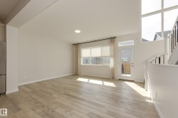 Spacious interior featuring light wood-finish flooring, a large window with roller shades, and a glass-paneled exterior door - 