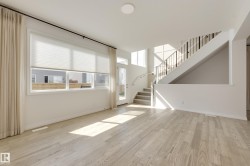 Open concept living space featuring light wood-finish flooring, a contemporary staircase with metal spindles, and a multi-pane glass door - 