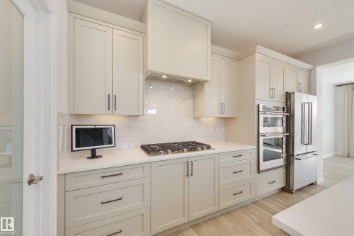 Kitchen featuring light-toned cabinetry with dark hardware, a gas cooktop, double wall ovens, and a side-by-side refrigerator - 3249 Dixon Way, Edmonton, AB 
