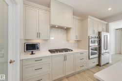 Kitchen featuring light-toned cabinetry with dark hardware, a gas cooktop, double wall ovens, and a side-by-side refrigerator - 