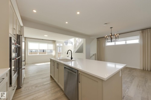 Kitchen featuring a central island with an undermount sink and matte black faucet, stainless steel appliances, recessed lighting, and light wood-finish flooring - 3249 Dixon Way, Edmonton, AB 