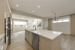 Kitchen featuring a central island with an undermount sink and matte black faucet, stainless steel appliances, recessed lighting, and light wood-finish flooring - 