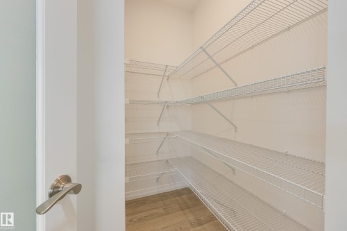 Walk-in pantry featuring extensive wire shelving, light wood-finish flooring, and a modern brushed nickel door handle - 3249 Dixon Way, Edmonton, AB 
