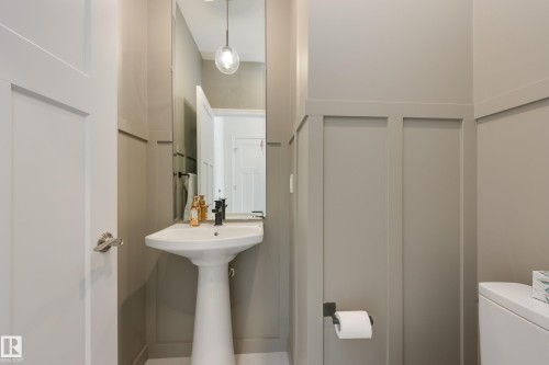 Contemporary powder room featuring a white pedestal sink with a matte black faucet, full-height wall mirror, modern pendant lighting, and wainscoting-style wall treatment - 3249 Dixon Way, Edmonton, AB 