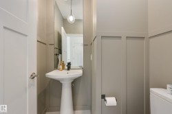 Contemporary powder room featuring a white pedestal sink with a matte black faucet, full-height wall mirror, modern pendant lighting, and wainscoting-style wall treatment - 