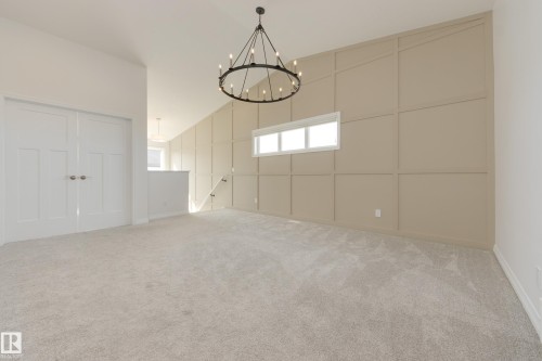 Spacious room featuring a decorative accent wall, a multi-pane horizontal window, and a large chandelier - 3249 Dixon Way, Edmonton, AB 