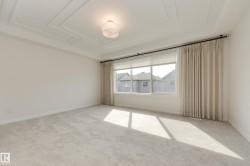 Spacious room featuring a coffered ceiling, a large window with roller shades and drapery, neutral carpeting, and a semi-flush mount ceiling fixture - 