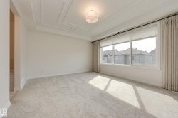 Spacious room featuring light-toned carpeting, a coffered ceiling, and a contemporary ceiling light fixture - 