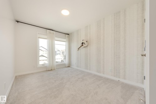 Bedroom featuring plush carpeting, two large windows with sheer white curtains, a patterned accent wall, recessed ceiling lighting, and crisp white baseboards - 3249 Dixon Way, Edmonton, AB 