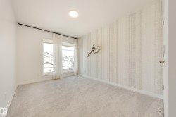Bedroom featuring plush carpeting, two large windows with sheer white curtains, a patterned accent wall, recessed ceiling lighting, and crisp white baseboards - 