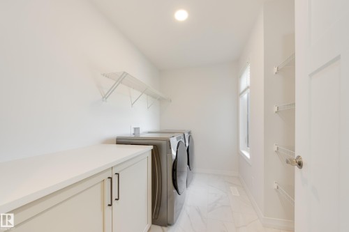 Dedicated laundry area featuring a built-in countertop, light-toned cabinetry with dark hardware, a window for natural light, and tile flooring - 3249 Dixon Way, Edmonton, AB 