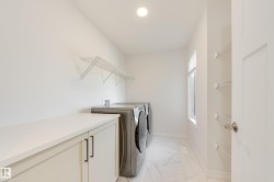 Dedicated laundry area featuring a built-in countertop, light-toned cabinetry with dark hardware, a window for natural light, and tile flooring - 