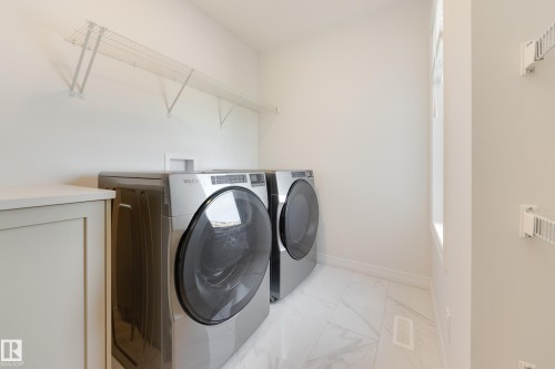 Dedicated laundry area featuring modern appliances, wire shelving, a built-in cabinet with countertop, and large format marble-look tile flooring - 3249 Dixon Way, Edmonton, AB 