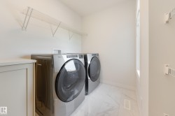 Dedicated laundry area featuring modern appliances, wire shelving, a built-in cabinet with countertop, and large format marble-look tile flooring - 