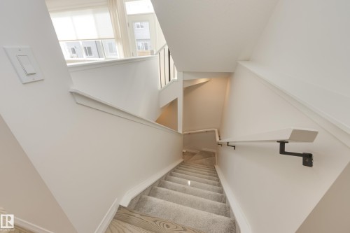 Split-level staircase featuring light wood-finish flooring, a carpeted runner, and a minimalist wall-mounted handrail with dark metal brackets - 3249 Dixon Way, Edmonton, AB 