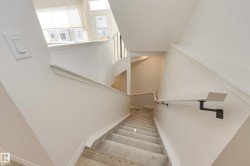 Split-level staircase featuring light wood-finish flooring, a carpeted runner, and a minimalist wall-mounted handrail with dark metal brackets - 