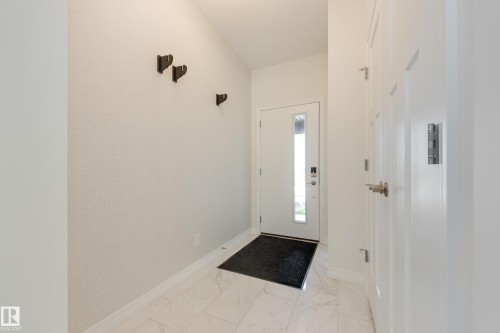 Entryway featuring white panel doors, modern door hardware, wall-mounted coat hooks, and white tile flooring - 3249 Dixon Way, Edmonton, AB 