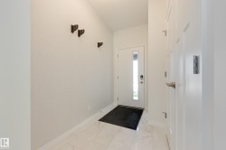 Entryway featuring white panel doors, modern door hardware, wall-mounted coat hooks, and white tile flooring - 