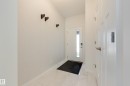 Entryway featuring white panel doors, modern door hardware, wall-mounted coat hooks, and white tile flooring - 3249 Dixon Way, Edmonton, AB 