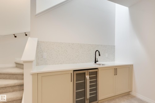 Built-in wet bar featuring a beverage cooler, light-toned cabinetry, a white countertop, and a speckled backsplash - 3249 Dixon Way, Edmonton, AB 
