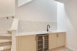 Built-in wet bar featuring a beverage cooler, light-toned cabinetry, a white countertop, and a speckled backsplash - 