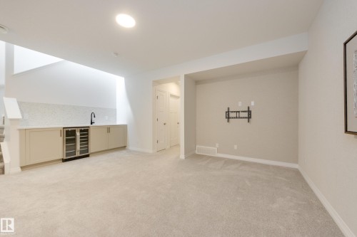 Finished lower-level space featuring light-colored carpeting and a built-in wet bar with a beverage cooler - 3249 Dixon Way, Edmonton, AB 