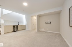 Finished lower-level space featuring light-colored carpeting and a built-in wet bar with a beverage cooler - 