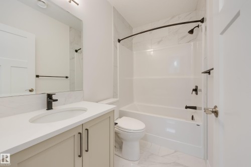Contemporary bathroom featuring a light-toned vanity with dark hardware, a white countertop with an integrated sink, and matte black fixtures - 3249 Dixon Way, Edmonton, AB 