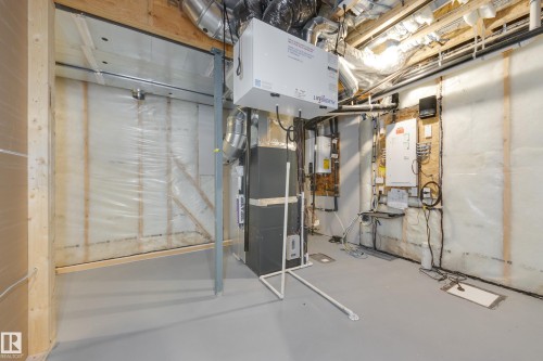 Utility room featuring exposed ceiling joists and ductwork, a floor-mounted furnace, and a wall-mounted ventilation unit - 3249 Dixon Way, Edmonton, AB 