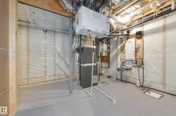 Utility room featuring exposed ceiling joists and ductwork, a floor-mounted furnace, and a wall-mounted ventilation unit - 
