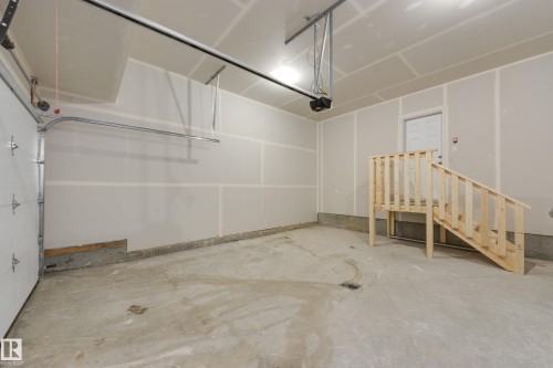 Spacious garage featuring a concrete floor, an overhead garage door, interior access door, and a built-in wooden staircase - 3249 Dixon Way, Edmonton, AB 