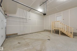 Spacious garage featuring a concrete floor, an overhead garage door, interior access door, and a built-in wooden staircase - 