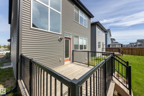 Rear exterior featuring gray horizontal siding, a private deck with black metal railing, and a red exterior door - 3249 Dixon Way, Edmonton, AB 