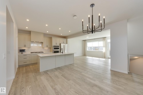 Open-concept kitchen and living area featuring wood-finish flooring, a contemporary island with seating, recessed lighting, and a modern chandelier - 3249 Dixon Way, Edmonton, AB 
