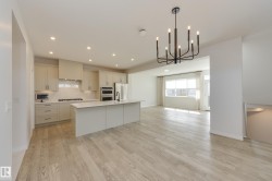Open-concept kitchen and living area featuring wood-finish flooring, a contemporary island with seating, recessed lighting, and a modern chandelier - 