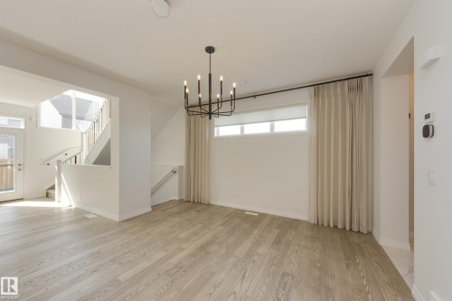 Spacious interior featuring wood-finish flooring, a modern black chandelier, and white window blinds - 3249 Dixon Way, Edmonton, AB 