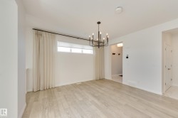 Spacious room featuring light wood-finish flooring, a modern black chandelier, and a large window with roller shades - 
