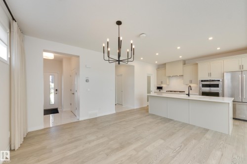 Open-concept living space featuring wood-finish flooring, a modern chandelier, recessed lighting, a kitchen island with a single-basin sink, and stainless steel appliances - 3249 Dixon Way, Edmonton, AB 