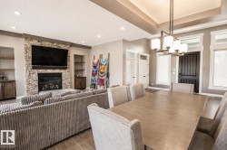 Open-concept living area featuring wood-finish flooring, a stone-faced fireplace with a hearth, and built-in shelving - 