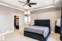 Neutral-toned bedroom featuring a tray ceiling with recessed lighting and a ceiling fan, plush carpeting, and a doorway to a walk-in closet - 